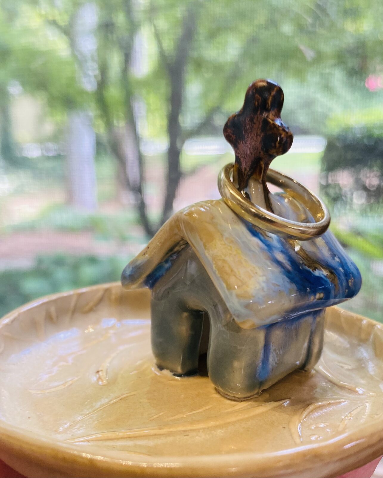 Whimsical ceramic house sculpture with a tree on top, glazed in blue and gold, sitting on a small dish