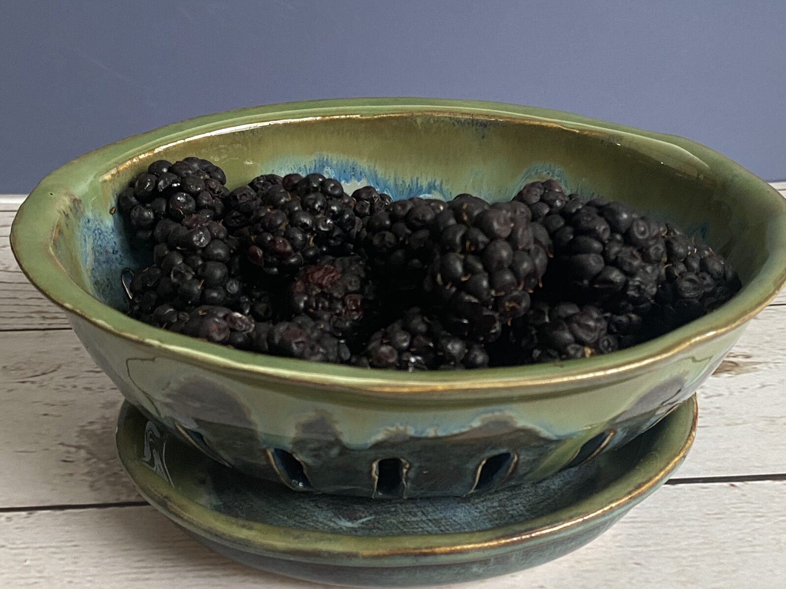 Green and blue glazed berry bowl on a matching plate, filled with fresh blackberries