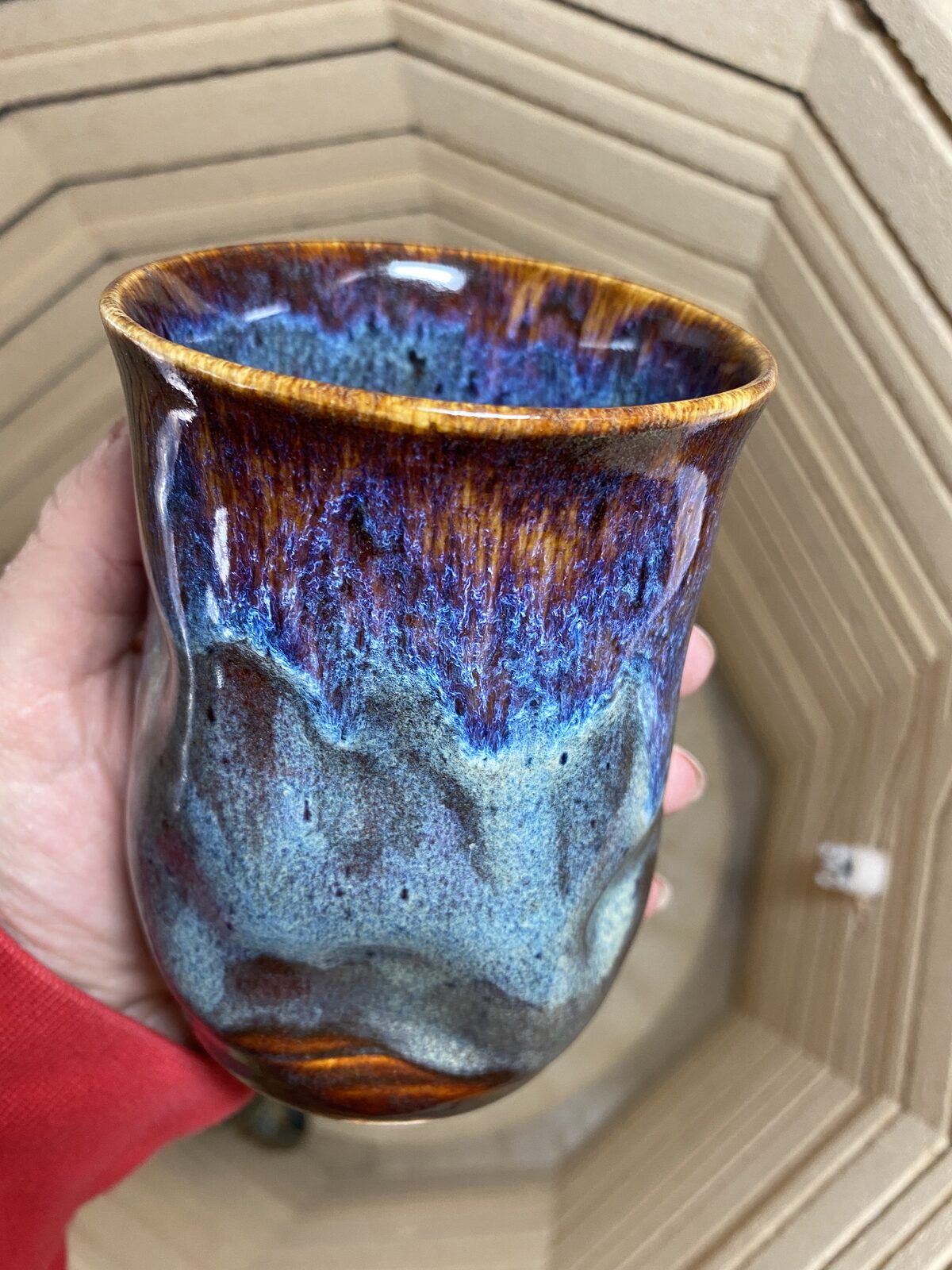 Curvy hand-thrown tumbler with amber, purple, and blue drip glaze