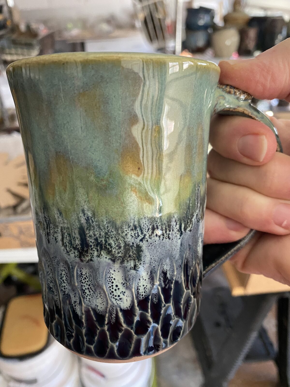 Tall mug with layered green and amber glaze fading into deep blue textured surface at the base
